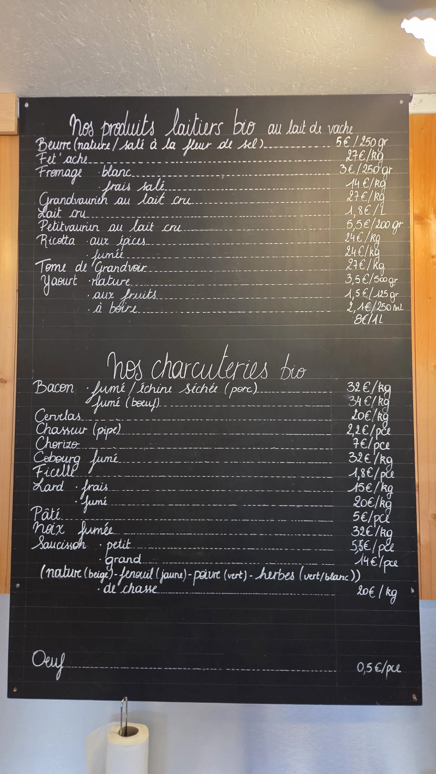 Ardoise écrite à la craie blanche listant les produits laitiers bio au lait de vache : beurre, fromage blanc, grandvaurien, petitvaurien, ricotta, yaourts, avec leurs prix